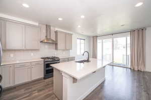 Kitchen with range with two ovens, a kitchen island with sink, gray cabinets, dark wood-style floors, and recessed lighting
