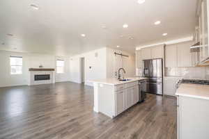 Kitchen with a barn door, stainless steel appliances, a kitchen island with sink, open floor plan, and tasteful backsplash