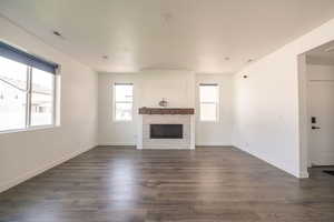 Unfurnished living room with dark wood-style floors and a glass covered fireplace