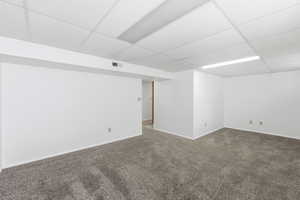 Unfurnished room featuring a drop ceiling and dark carpet
