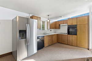 Kitchen with black appliances, light countertops, wood finish cabinetry, and decorative light fixtures