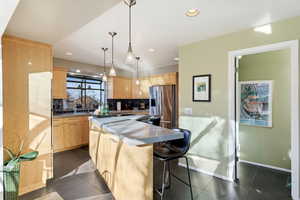 Kitchen featuring light wood finish cabinets, stainless steel refrigerator with ice dispenser, a kitchen island, hanging light fixtures, and a breakfast bar