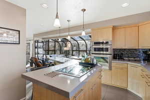 Kitchen featuring light wood finish cabinets, a center island, stainless steel double oven, electric cooktop, and hanging light fixtures