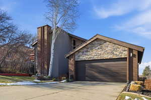 View of front of house featuring a garage, driveway, stone siding, and brick siding