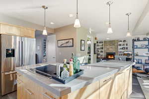 Kitchen featuring light wood finish cabinets, stainless steel refrigerator with ice dispenser, black electric stovetop, a tile fireplace, and modern cabinets
