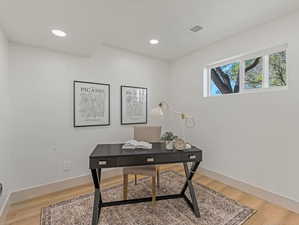 Home office with light wood finished floors and recessed lighting