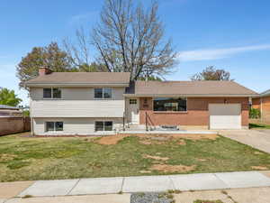 Split level home with a front yard, a garage, driveway, a tiled roof, and a chimney