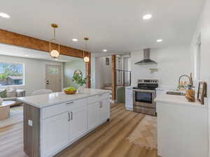 Kitchen with electric stove, light stone counters, light wood-style flooring, white cabinets, and a kitchen island