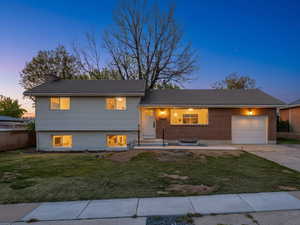Split level home featuring a garage, a front lawn, driveway, a porch, and a chimney