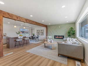 Living room with light wood-style floors, a glass covered fireplace, recessed lighting, and an accent wall
