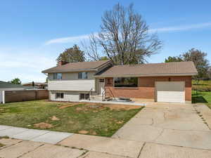 Split level home with a front lawn, concrete driveway, brick siding, and an attached garage