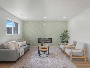 Living room featuring a decorative wall, an accent wall, light wood-style floors, a glass covered fireplace, and recessed lighting