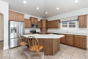Kitchen featuring stainless steel appliances, light countertops, wood finish cabinetry, a center island, and recessed lighting