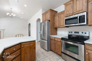 Kitchen featuring stainless steel appliances, light countertops, wood finish cabinets, lofted ceiling, and arched walkways