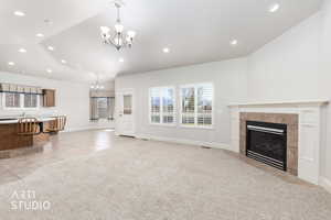 Unfurnished living room featuring hanging lights, vaulted ceiling, light colored carpet, a tile fireplace, and light tile patterned flooring