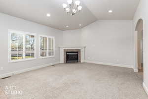Unfurnished living room featuring arched walkways, lofted ceiling, light colored carpet, a fireplace, and suspended lighting