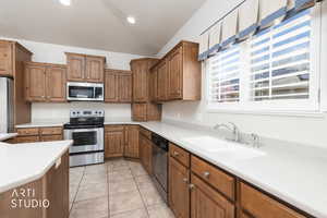 Kitchen with stainless steel appliances, light countertops, wood finish cabinets, light tile patterned floors, and vaulted ceiling