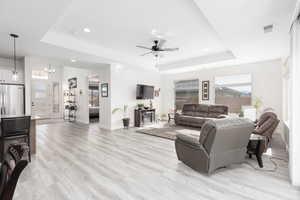 Living area featuring ceiling fan, light wood-style floors, a tray ceiling, and hanging lights
