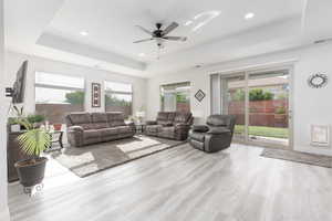 Living room featuring a ceiling fan, a tray ceiling, plenty of natural light, light wood-style flooring, and recessed lighting