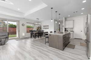 Kitchen with light stone counters, two tone cabinetry, a kitchen breakfast bar, decorative light fixtures, and an island with sink