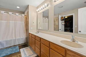 Full bath featuring double vanity, a spacious closet, shower / bath combo with shower curtain, and dark stone finish floors