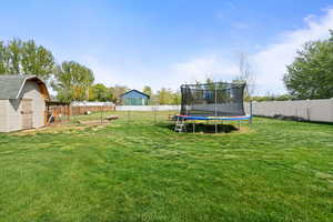 Fenced backyard featuring a trampoline, a playground, and a storage shed