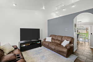 Living room with arched walkways, lofted ceiling, stone tile flooring, and recessed lighting