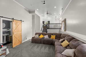 Living room featuring ornamental molding, a barn door, ceiling fan, carpet flooring, and recessed lighting