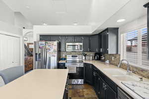 Kitchen with stainless steel appliances, decorative backsplash, dark cabinets, arched walkways, and dark stone finish flooring