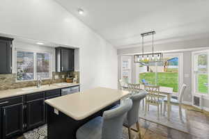Kitchen with dark cabinetry, vaulted ceiling, light countertops, and backsplash