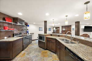 Kitchen with black appliances, light stone counters, dark wood finish cabinets, and decorative light fixtures
