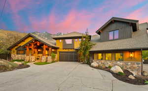 Craftsman-style home with stone siding, roof with shingles, driveway, and a garage