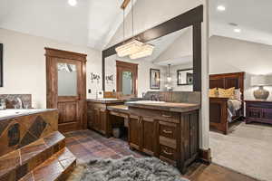 Ensuite primary bedroom bathroom with recessed lighting, double vanity, stone tile floors, a garden tub, and lofted ceiling