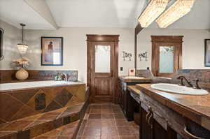 Bathroom featuring stone tile flooring, hanging lights, vanity, and a bath