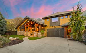 View of front of home featuring roof with shingles, concrete driveway, a garage, stone siding, and stucco siding