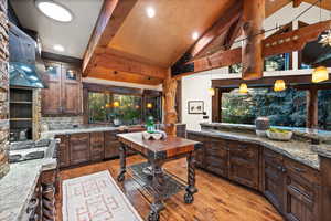 Kitchen with dark wood finish cabinets, light wood finished floors, pendant lighting, dark stone countertops, and vaulted ceiling
