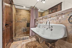 Full bath with stone tile floors, a shower stall, and tile walls