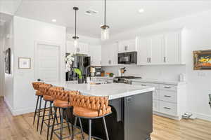Kitchen with a kitchen island with sink, a kitchen bar, stainless steel appliances, light wood-style floors, and light stone countertops
