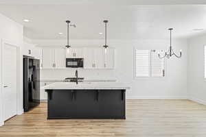 Dual tone kitchen with a breakfast bar area, a center island with sink, light wood-type flooring, black appliances, and two tone color scheme
