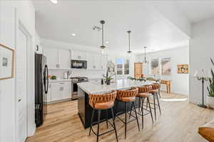 Kitchen with black appliances, a breakfast bar area, light wood-style floors, an island with sink, and light stone countertops