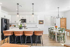 Two tone kitchen with a breakfast bar, a center island with sink, black appliances, light wood-style flooring, and light stone countertops