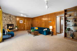 Living room featuring rail lighting, a stone fireplace, light colored carpet, and wooden walls