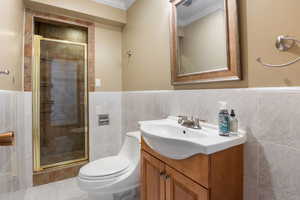 Full bathroom with vanity, ornamental molding, a shower stall, and tile walls