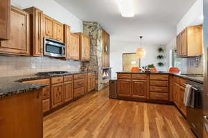 Kitchen with decorative backsplash, dark stone countertops, light wood-type flooring, and a peninsula