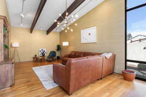 Living room with light wood-style flooring, beam ceiling, suspended lighting, and wallpapered walls