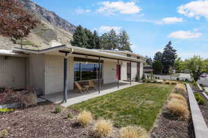 Rear view of house featuring a chimney, brick siding, a lawn, a patio area, and a mountain view