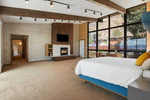 Bedroom with rail lighting, a tiled fireplace, carpet, beamed ceiling, and brick wall