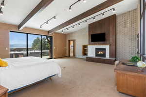 Bedroom with rail lighting, brick wall, light colored carpet, a fireplace, and access to outside