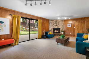 Carpeted living area featuring wood walls, track lighting, and a stone fireplace