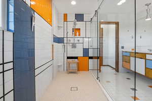 Bathroom featuring tile walls, a stall shower, vanity, light tile patterned flooring, and recessed lighting